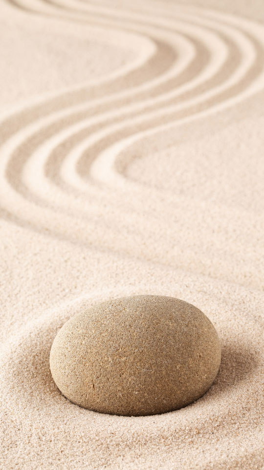 Runder Stein auf hellem Sand mit geschwungenen Rillen, wie in einem Zen-Garten