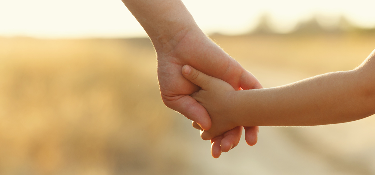Erwachsene Hand hält Kinderhand im Gegenlicht